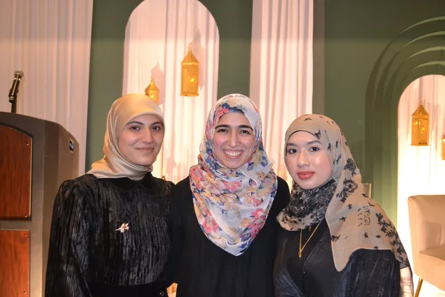 Three students standing by the green stage arches