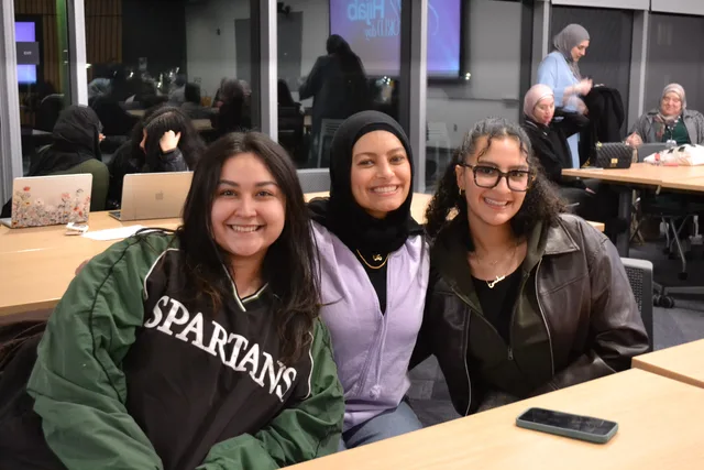 Three students smiling together at a classroom table