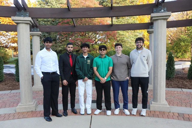 Six students posing beneath a pergola in autumn